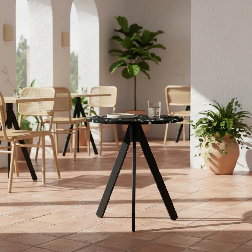Black eco-friendly table with tripod base and recycled plastic top on a Mediterranean-style terrace, surrounded by rattan chairs
