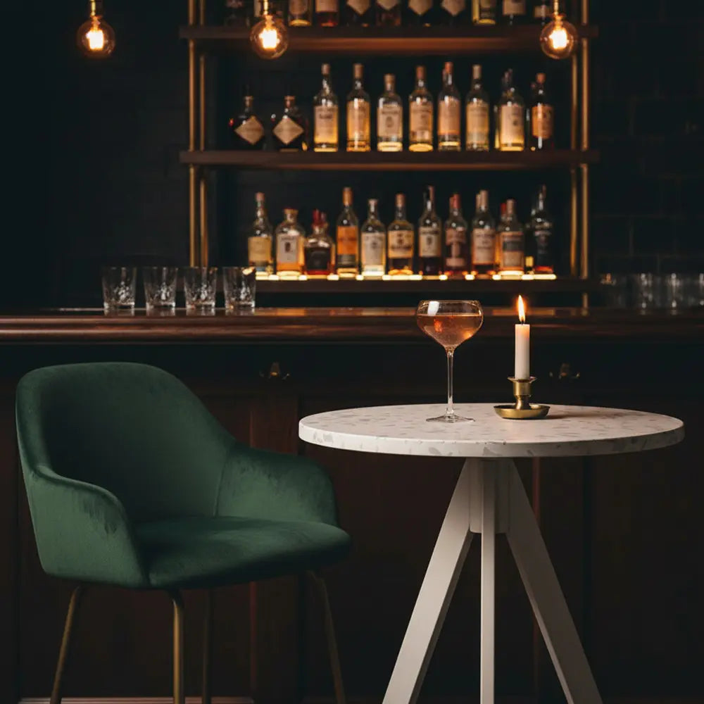 Round white eco-friendly table with recycled plastic top in an upscale bar, paired with a green velvet armchair and lit candle