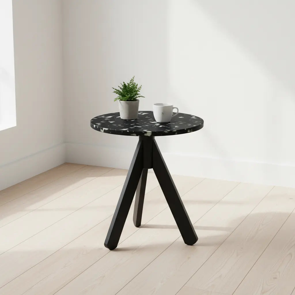 Black recycled plastic side table with tripod base, styled with a potted plant and white mug in a bright minimalist interior